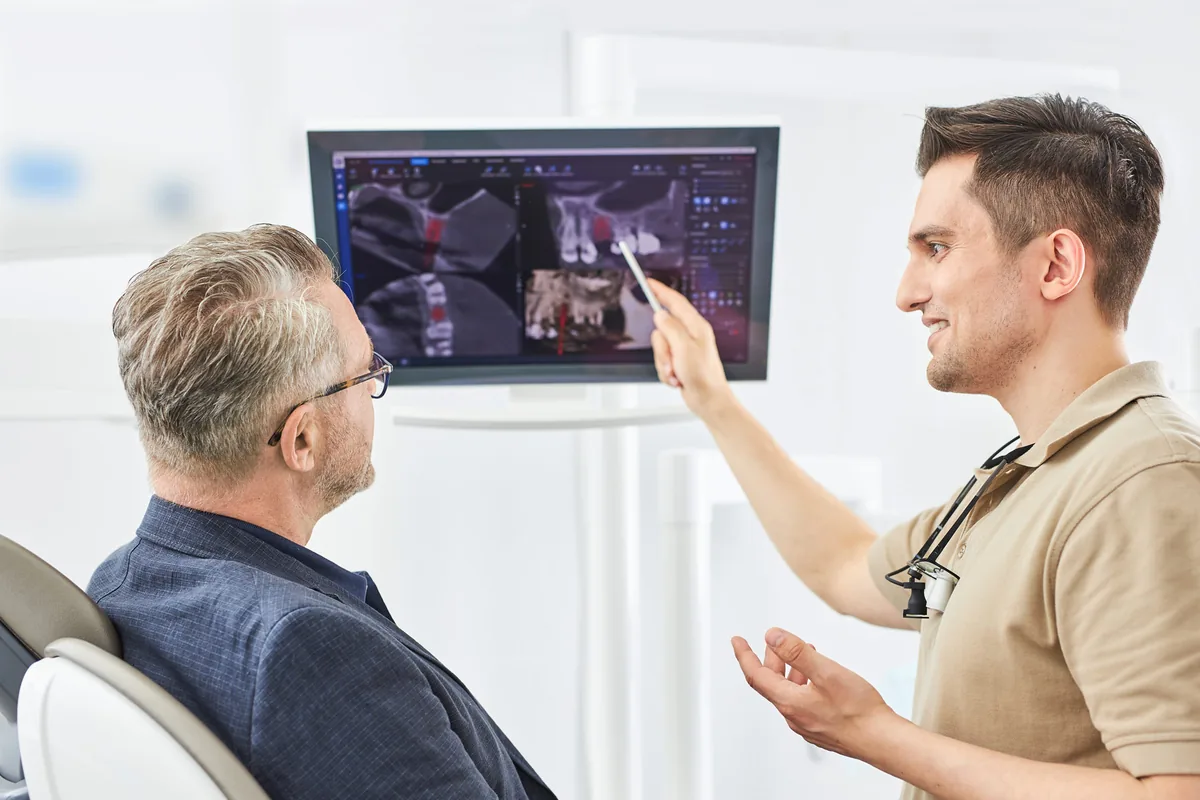 Dr. Dzenan Barking erklärt einem Patienten im Zahnwohl Calw die digitale Implantatplanung am Bildschirm